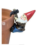 A small garden gnome Pot Sitter figurine with a red hat, white beard, and blue pants, holding a black pickaxe and leaning against a terracotta pot on a white background.