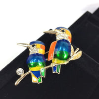 Beautiful colourful birds on a branch in blues, yellow greens and orange.